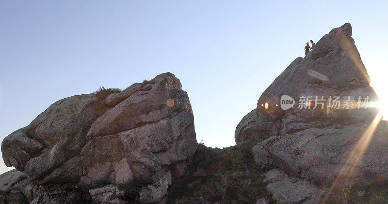 远处两名攀登者登上岩壁顶峰，日出的景象