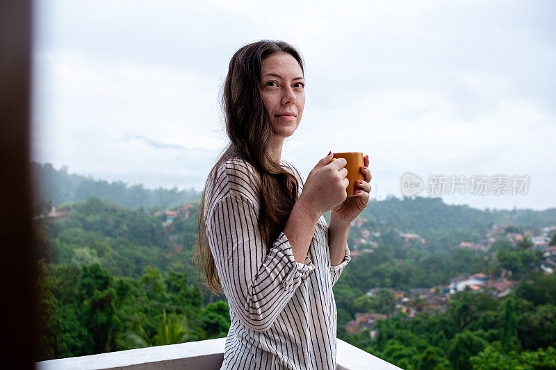 一名年轻女子在山顶上喝着茶，背景是全景