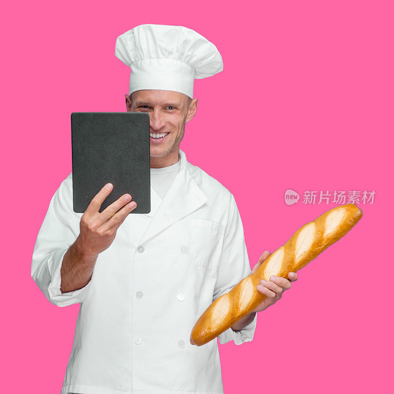 白人年轻男性面包师站在有色背景前，穿着裤子，拿着面包，用数码平板电脑