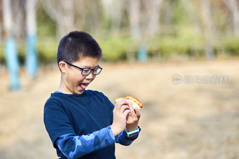 快乐的东亚男孩正在户外吃面包