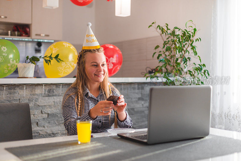 在封锁期间，一名年轻的金发女子在她的笔记本电脑前拿着一个临时制作的生日蛋糕庆祝她的生日