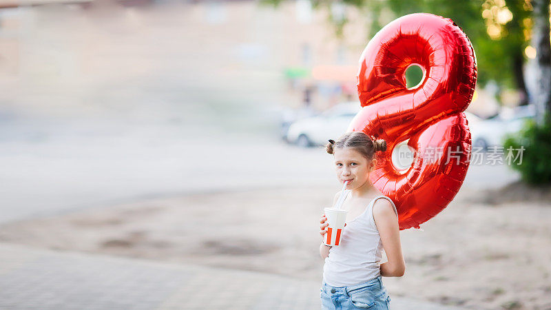 欧洲女孩用8型气球和苏打水，用吸管。孩子夏天在外面用吸管喝汽水