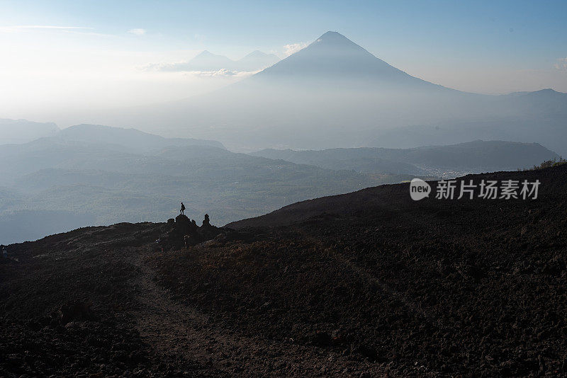 危地马拉，一名男子站在两座火山前的一块火山岩上