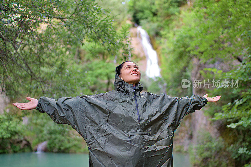 女人穿着雨衣，举起双手欣赏大自然