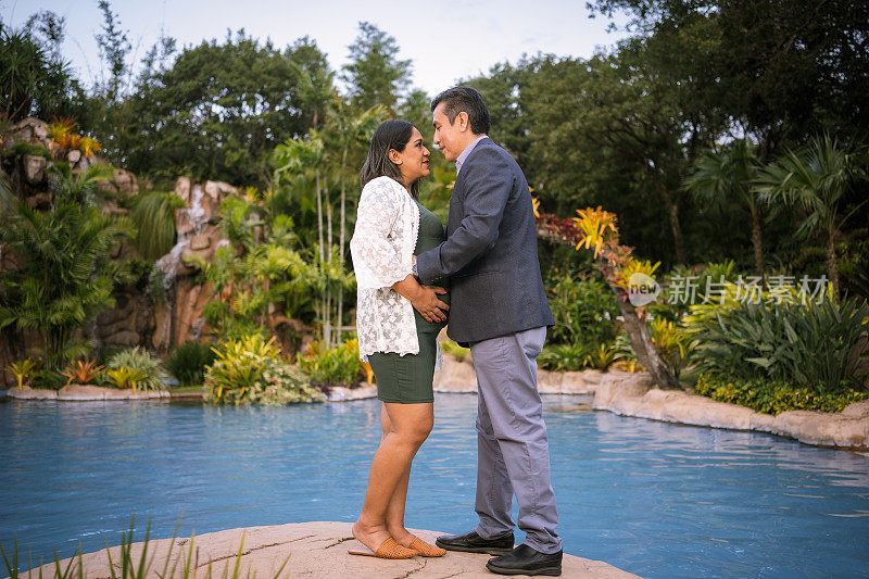 丈夫在被热带丛林包围的游泳池旁看着他怀孕的妻子