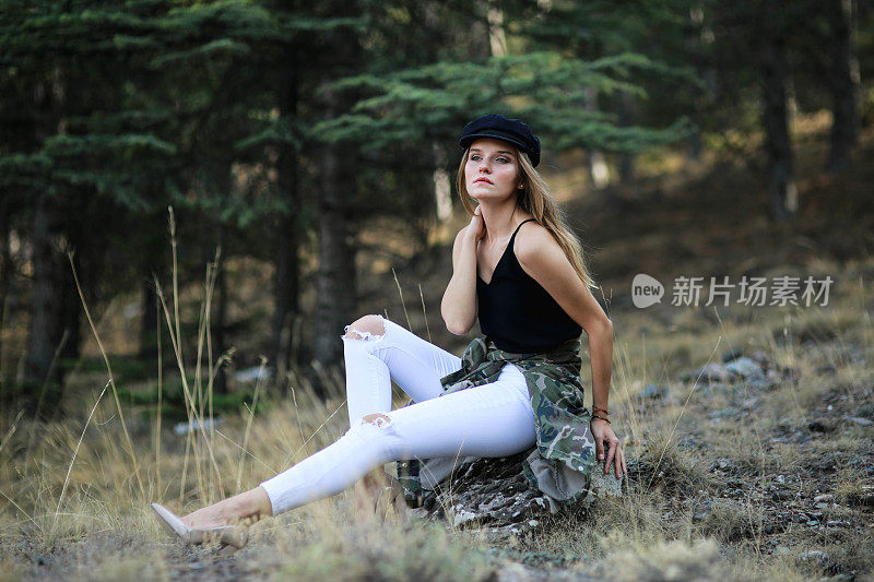 年轻的金发女子戴着帽子在松树丛中摆姿势。拍摄时尚大片
