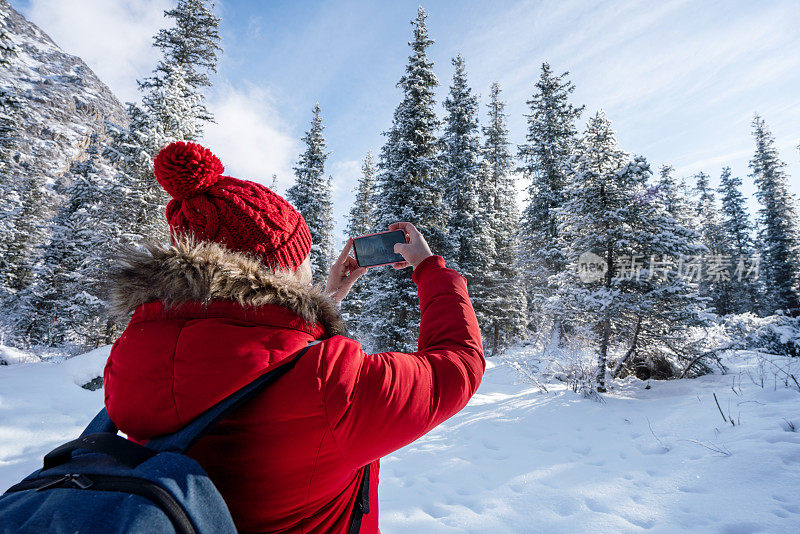 女游客背着背包拍摄雪山和森林