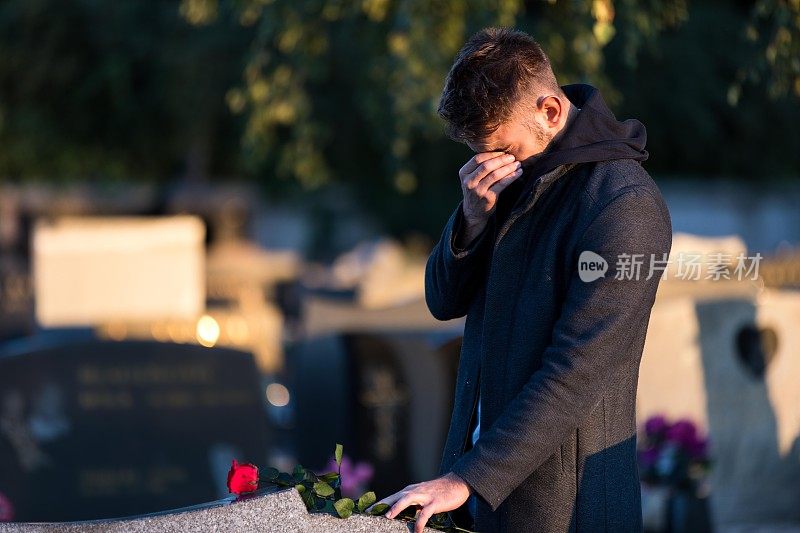 一个男人把一朵红玫瑰放在坟墓上的特写镜头