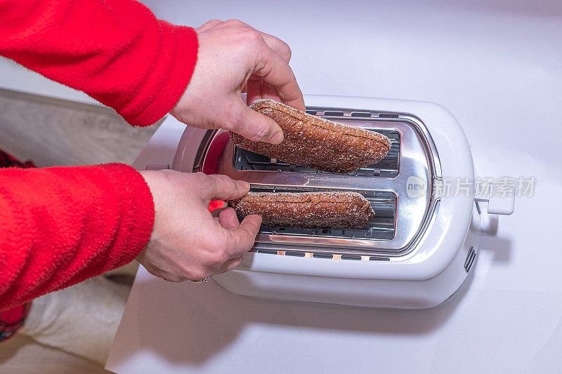 女人的手，一个女人在电烤面包机里准备烤面包。上角。