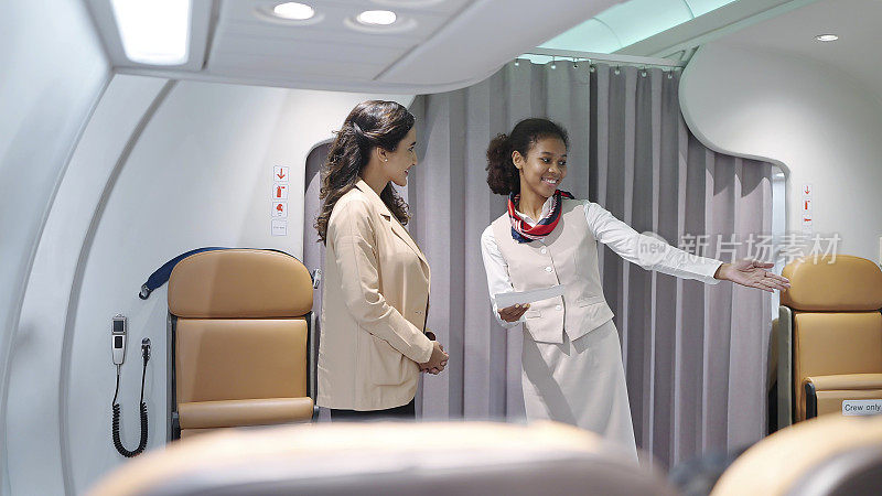穿着制服的年轻女乘务员站在飞机入口，微笑着检查乘客的登机牌，欢迎乘坐这架航班。航空公司运输