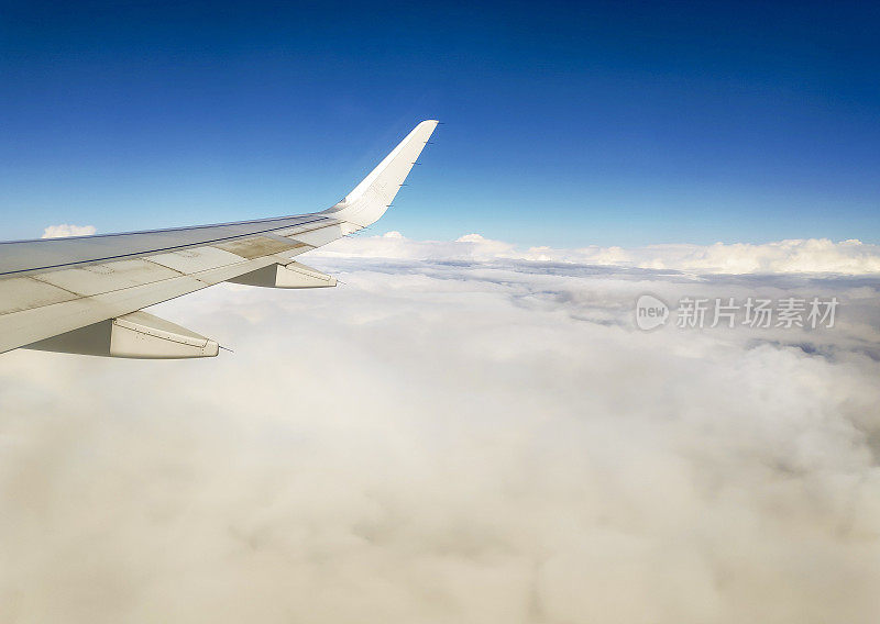 从飞机机翼的窗户看，在云层和蓝天上飞行。