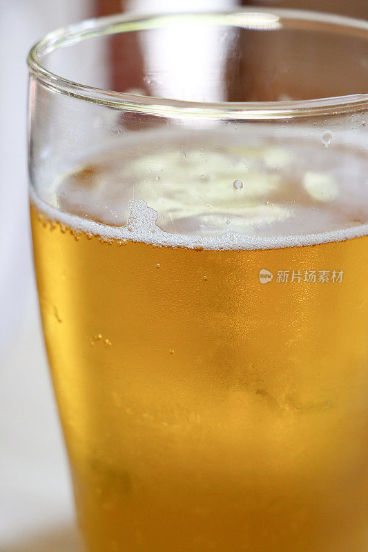 一品脱啤酒在玻璃上的特写图像覆盖了凝结与起泡的气泡形成泡沫的顶部啤酒，一品脱玻璃在酒吧的桌子上，重点在前景
