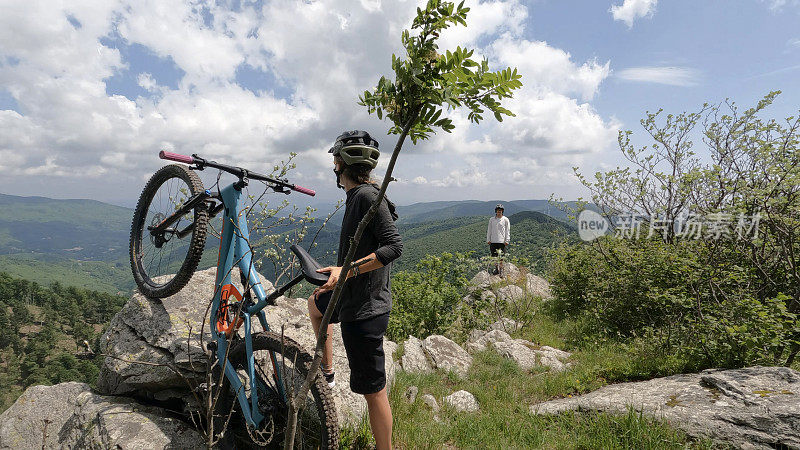 山地自行车手推着自行车俯瞰山谷、森林