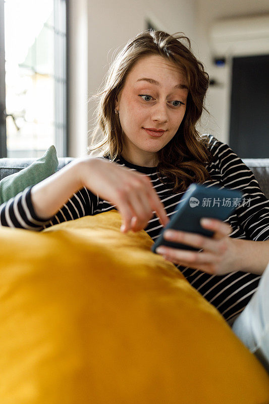 年轻女子懒洋洋地躺在沙发上，用智能手机上网