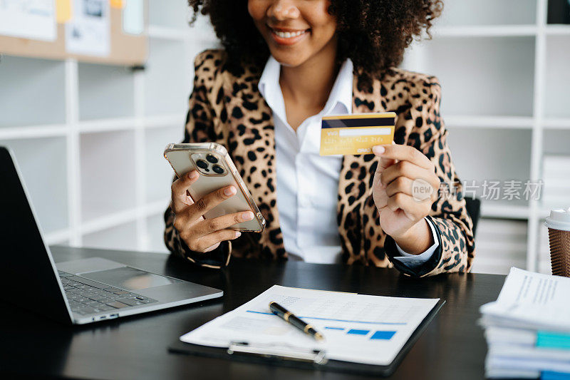 非洲妇女使用智能手机进行移动支付，网上购物，全渠道，坐在桌子上，虚拟图标图形界面屏幕