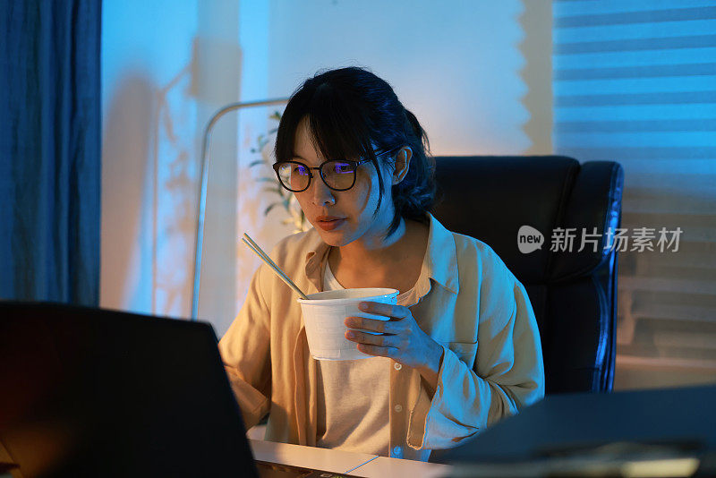 亚洲年轻女商人吃面条吃到深夜熬夜工作，工作时又忙又饿