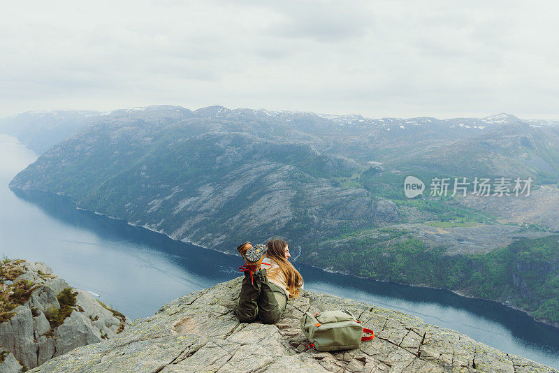 背着背包的女人在悬崖边放松，欣赏挪威吕瑟峡湾田园诗般的景色