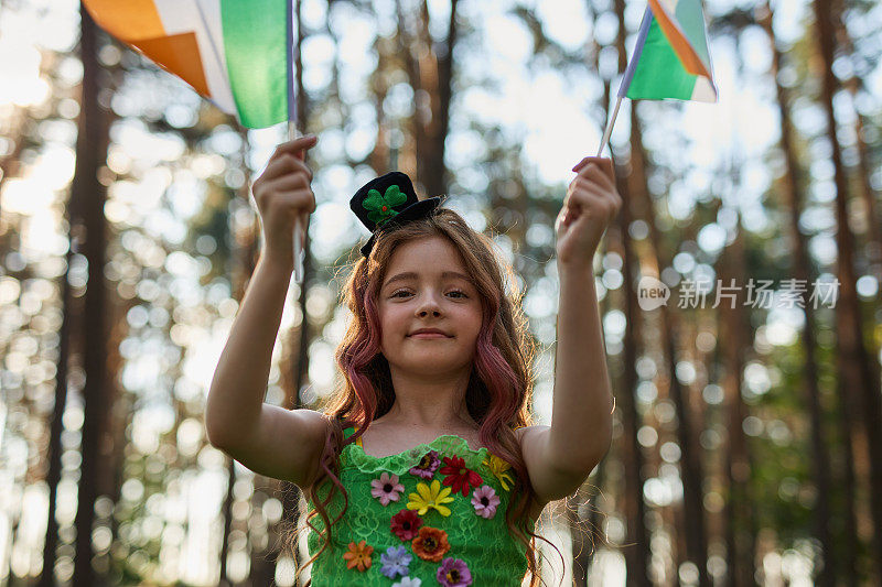 在圣帕特里克节上，一个红头发的漂亮小女孩穿着小妖精的衣服，挥舞着爱尔兰国旗
