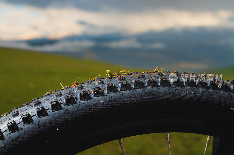 概念mtb下坡自行车主题。全地形山地自行车轮胎的胎面特写，背景是山脉和日落的天空
