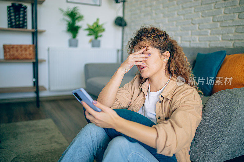 沮丧的女人拿着手机坐在地板上