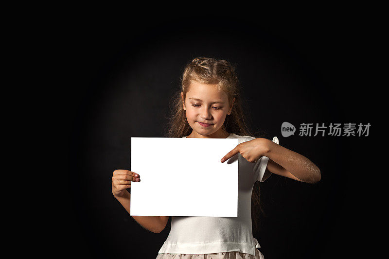 儿童女孩模型指向模板上，手握白纸留白，看上去很自信。可爱的封面孩子推广模型模板，工作室在阴影中拍摄。广告的概念。复制广告文本空间