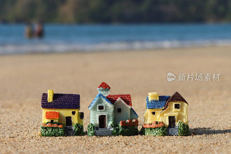 一排模型度假小屋的特写图像，坐落在阳光明媚的沙滩上，背景是退潮时的海浪，大海和海岸线，度假租赁和度假屋的概念，重点放在前景，复制空间