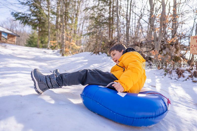 小男孩骑着雪管从山上滑下来