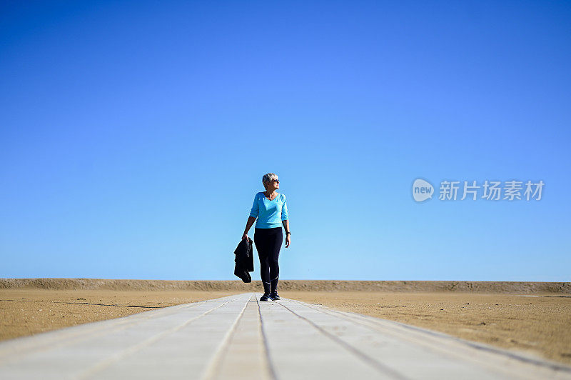 一个成熟的女人在晴朗的天空前走在沙滩上的低角度视图。