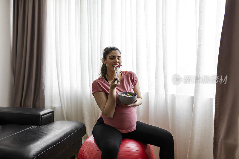 吃沙拉的孕妇，坐在健身球上