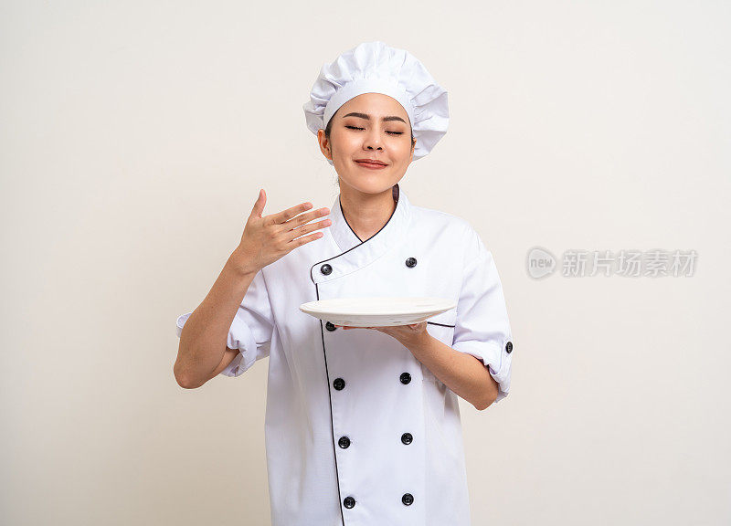 闻闻食物。漂亮的亚洲女厨师穿着制服，拿着盘子、勺子、器具在厨房里烹饪，各种姿势的菜单好好吃就孤立了。厨师女厨师人在厨房餐厅