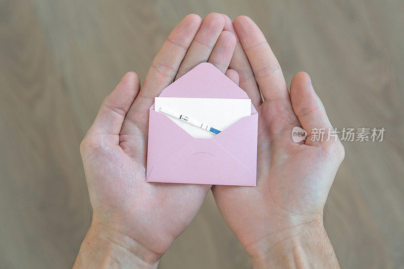男性手里拿着一个粉红色的信封，里面有一张白色的纸和一个阳性的怀孕测试