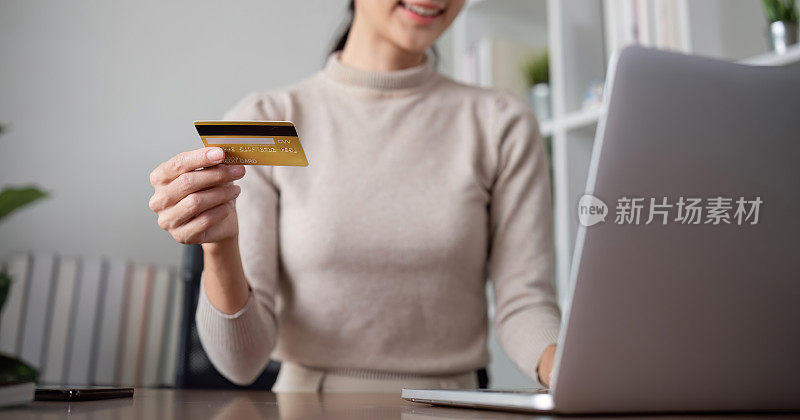 美丽的年轻女子用笔记本电脑上网购物，通过手机网上银行应用程序用信用卡购物和支付。