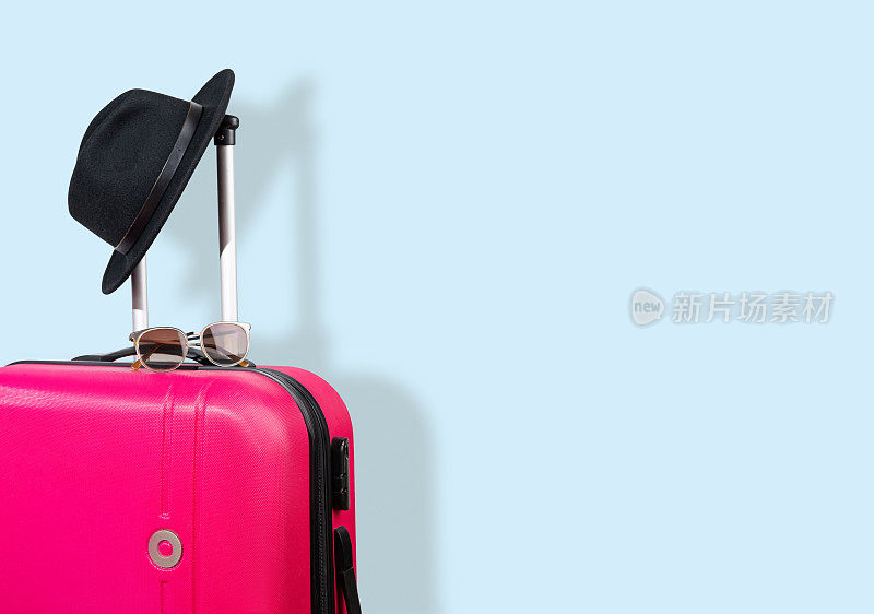 粉红色的行李箱和黑色的帽子在灰色的阴影背景上。