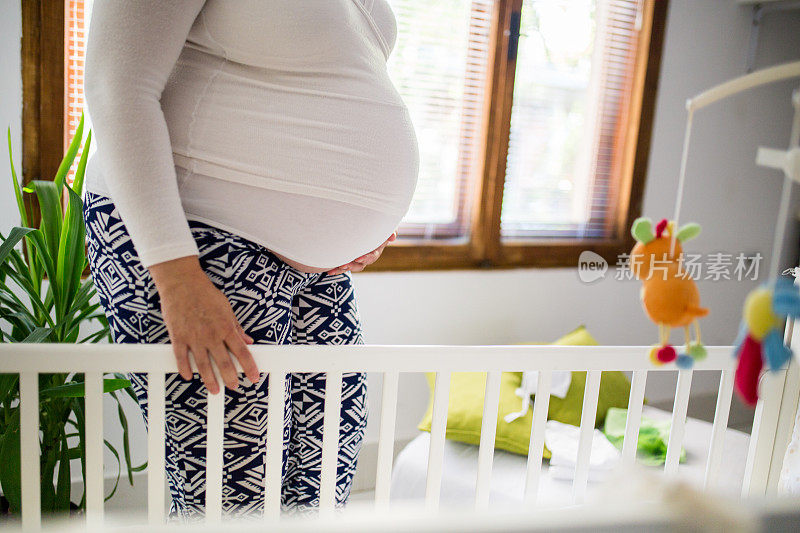 孕妇站在婴儿床旁摸肚子