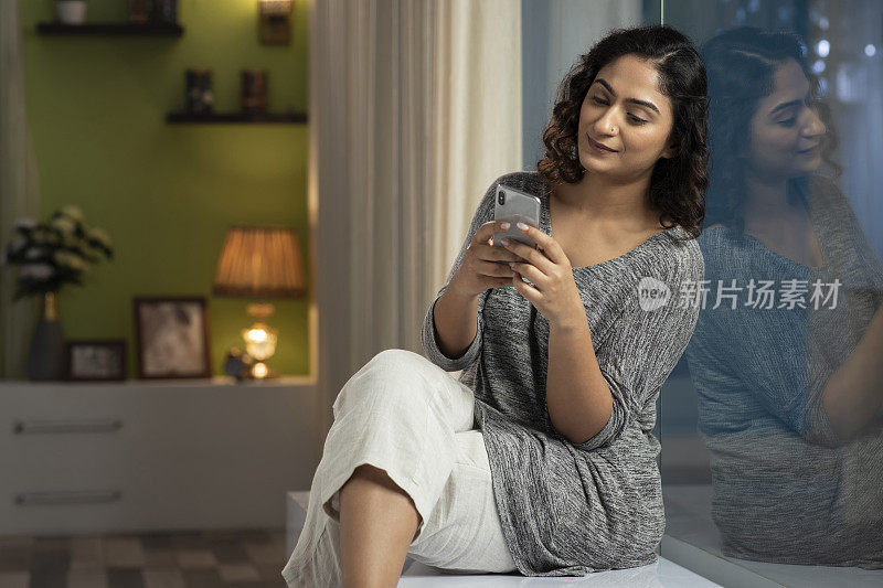 一个年轻女人坐在窗台上，在家里打电话，库存照片