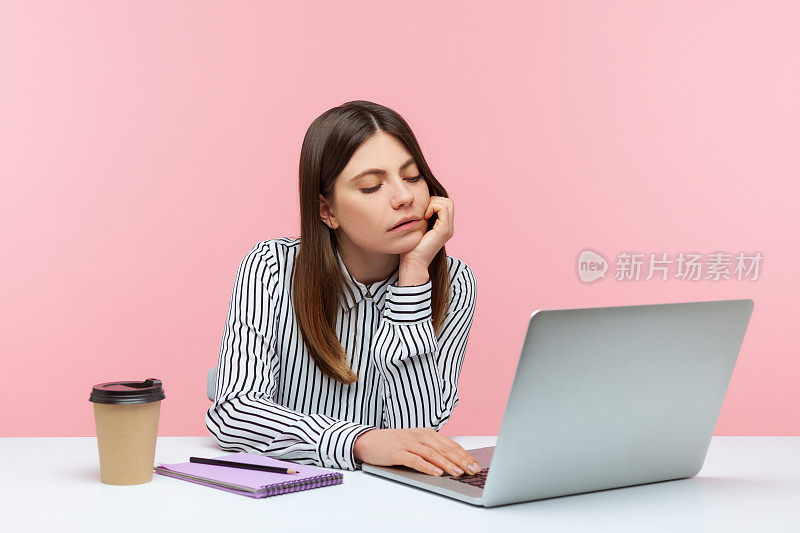 无聊不开心的商务女性坐在工作场所看着笔记本电脑屏幕进行视频通话，厌倦了在线会议，拖延症