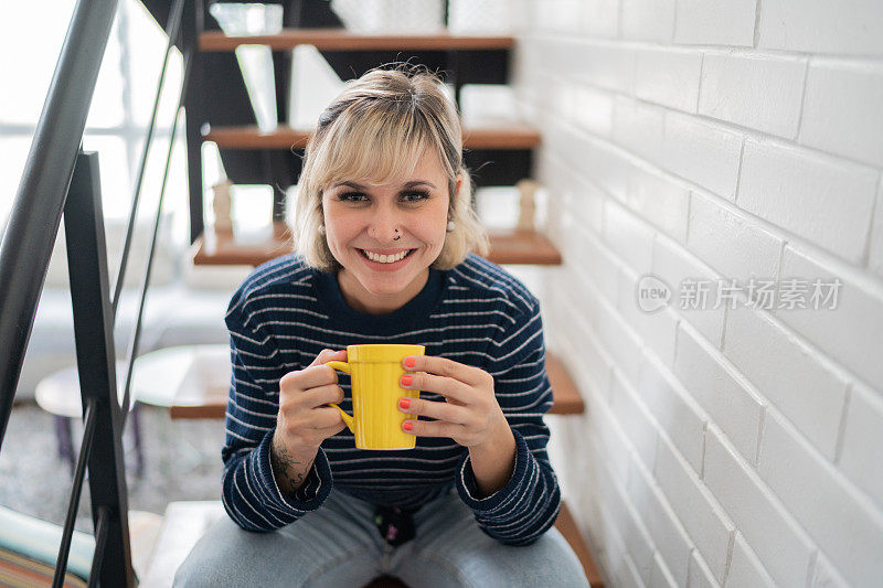 一个快乐的女人拿着茶杯坐在家里的楼梯上