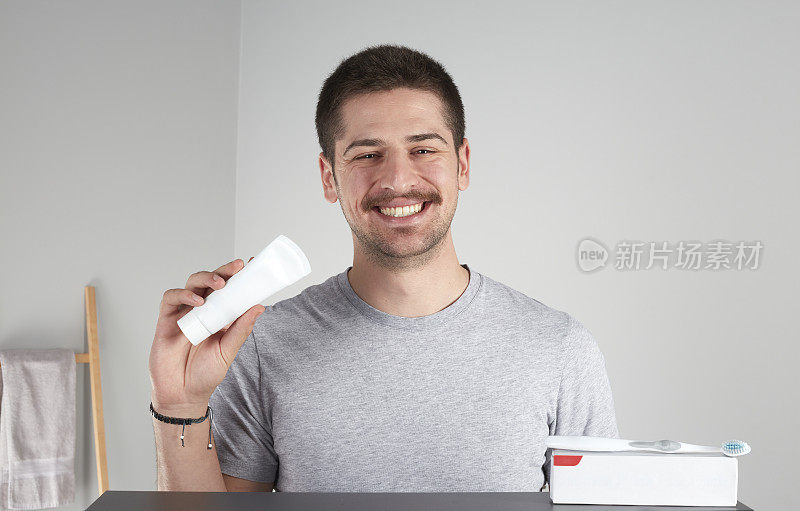 一个年轻人对着镜头微笑，展示着牙膏