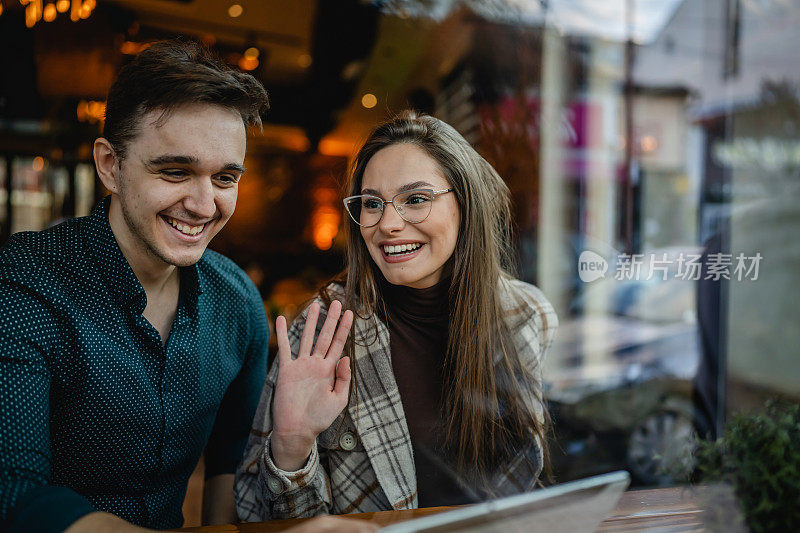 两个人年轻的成年夫妇女人和男人的男朋友和女朋友坐在咖啡馆快乐的微笑招手打招呼在天真实的人复制空间的关系概念