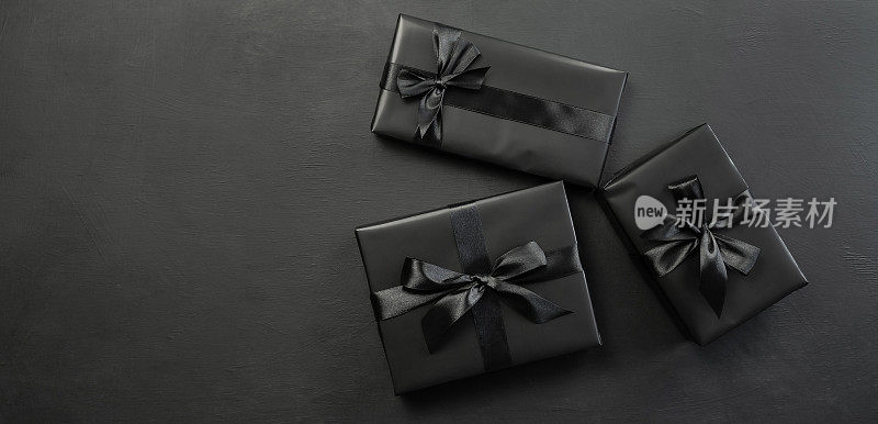 礼品盒用黑色的纸包装，黑色的背景上有一个黑色的蝴蝶结。节日的概念。“黑色星期五”。放置文字或广告的地方。