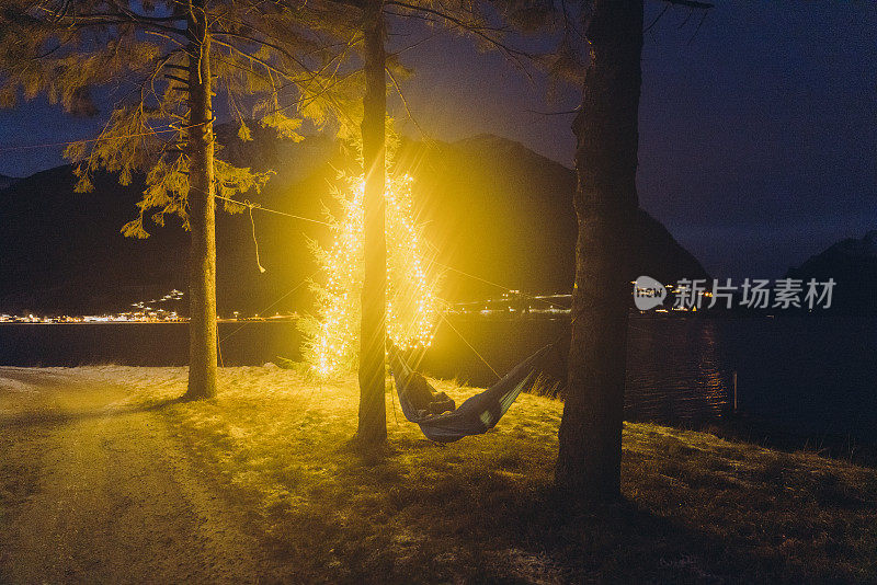 挪威，一名女子在圣诞树旁的吊床上放松，凝视着冬天的户外活动