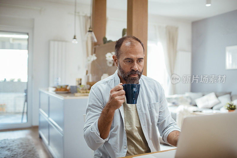 中年男子一边用笔记本电脑一边吃早餐