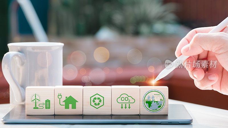 净零和碳中和的概念。Hand放置了带有netzero图标的木制立方体，用于废物回收、绿色生产、减少碳排放和可再生能源。绿色的背景