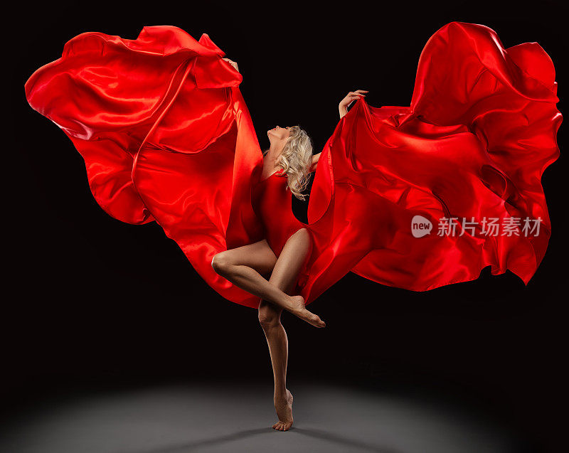 芭蕾舞者跳着红色的丝绸织物在风中飞过黑色背景。美丽的芭蕾舞演员在舞动的裙子与漂浮的围巾跳舞。现代舞表演