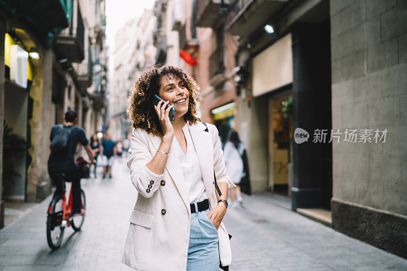 漂亮的女游客在时尚的服装走在城市的街道上，在漫游的国际智能手机对话中讨论独自度假的经历，快乐的女孩用手机聊天