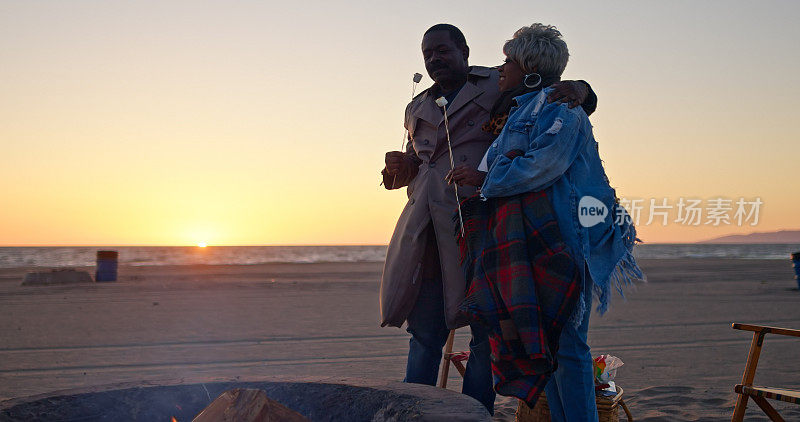 非裔美国老人夫妇享用烤棉花糖在日落海滩