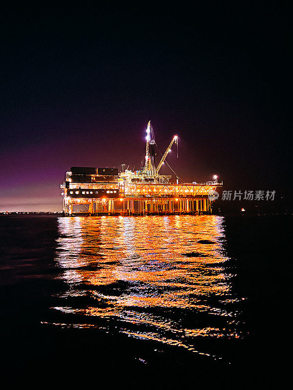 低角度移动照片照明，发光的石油钻井平台在太平洋的夜晚，灯光在水中的反射