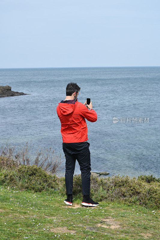 年轻的成年男子在海岸线用智能手机拍照