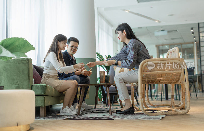 一名亚洲女商人在一间现代化的休息室里与顾客交换名片。库存图片