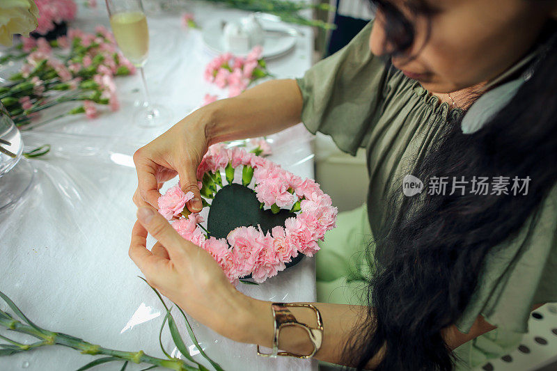 一位亚洲妇女正在上插花课，她用许多康乃馨做了一束心形的花，送给母亲庆祝母亲节。